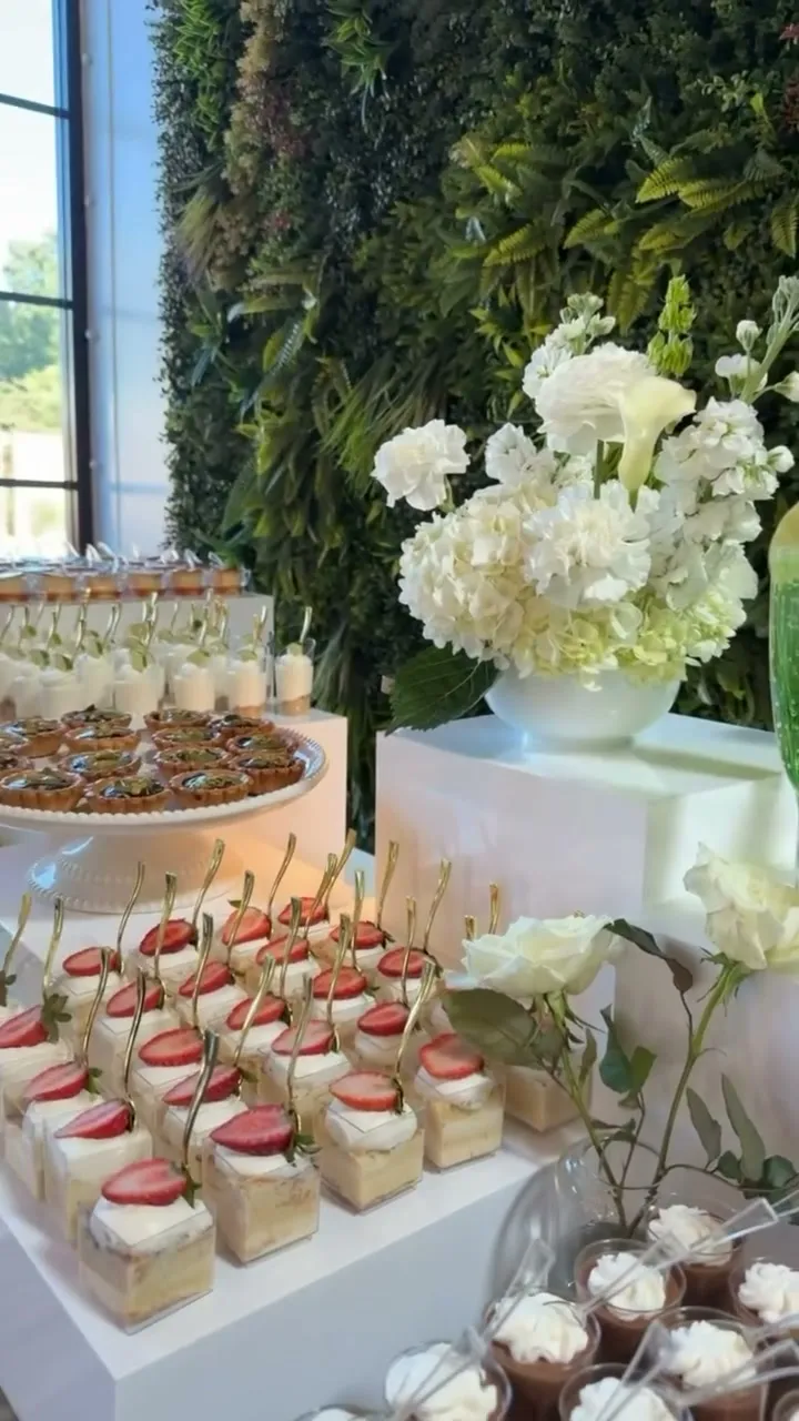 Dessert table with a greenery wall, white florals and strawberry shortcake cups